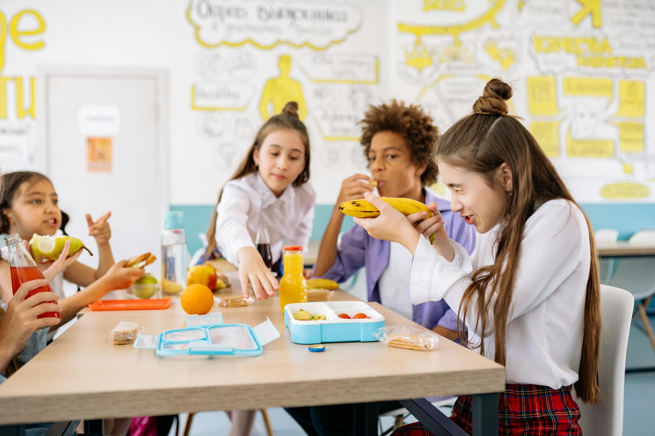 Group of students sharing healthy snacks and drinks in a vibrant school cafeteria setting.